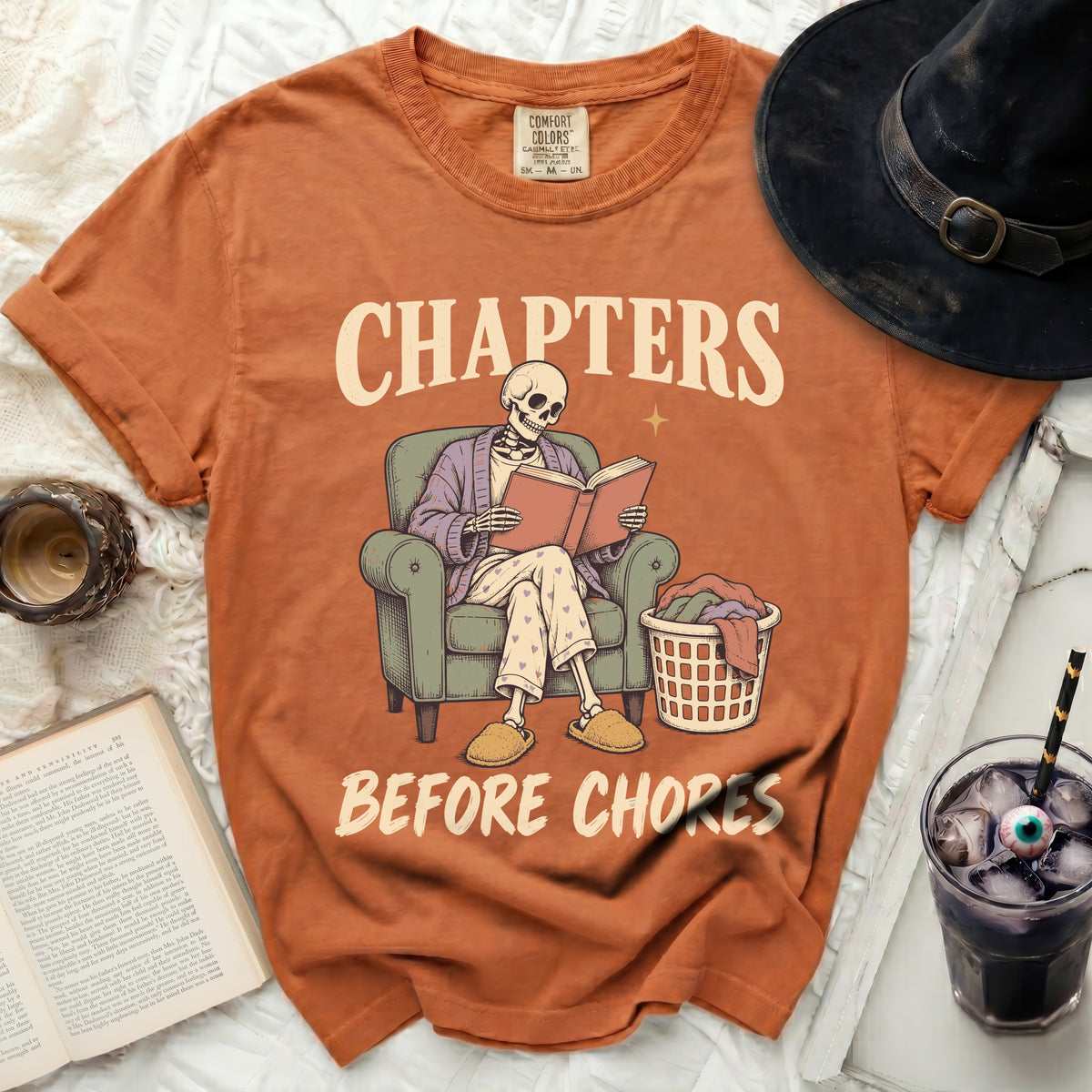 Orange t-shirt with skeleton reading book, "Chapters Before Chores" text.
