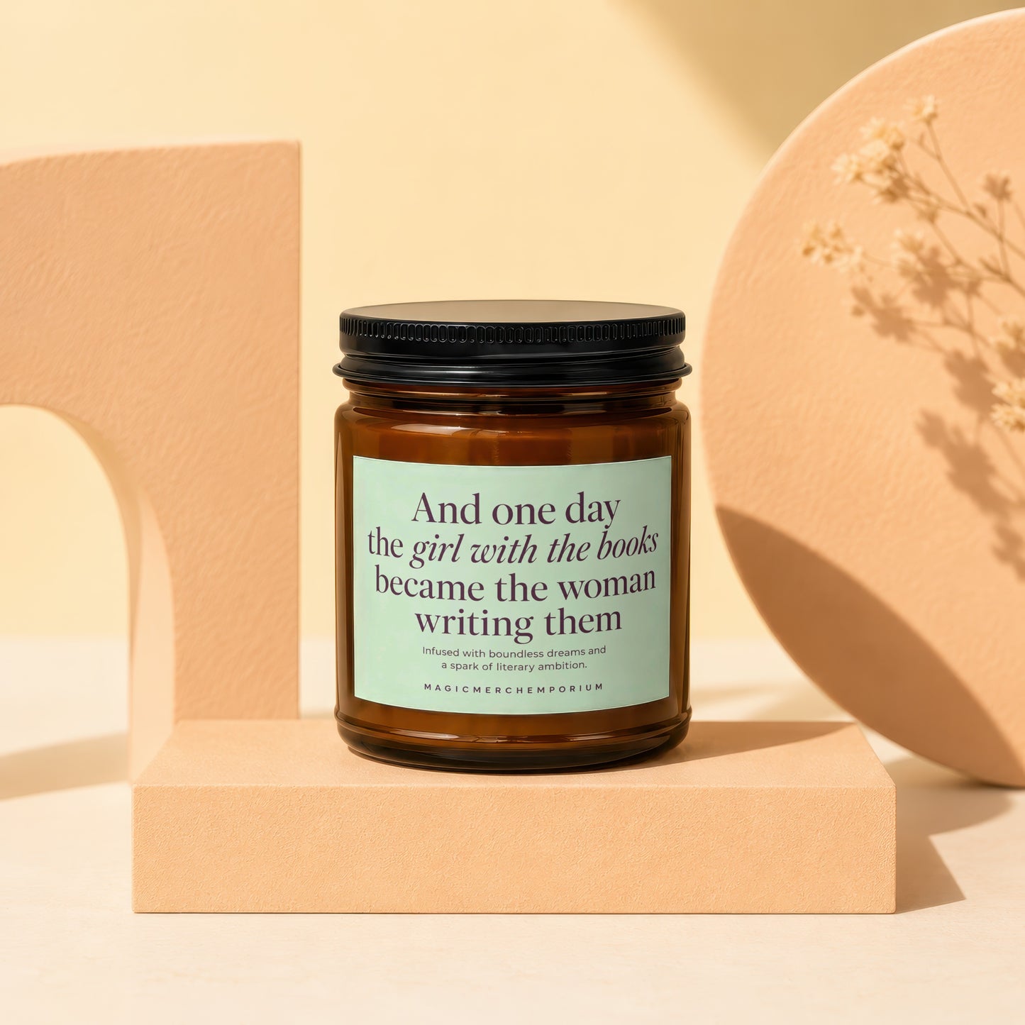 Amber jar candle with black lid, green label reads "And one day the girl with the books became the woman writing them".