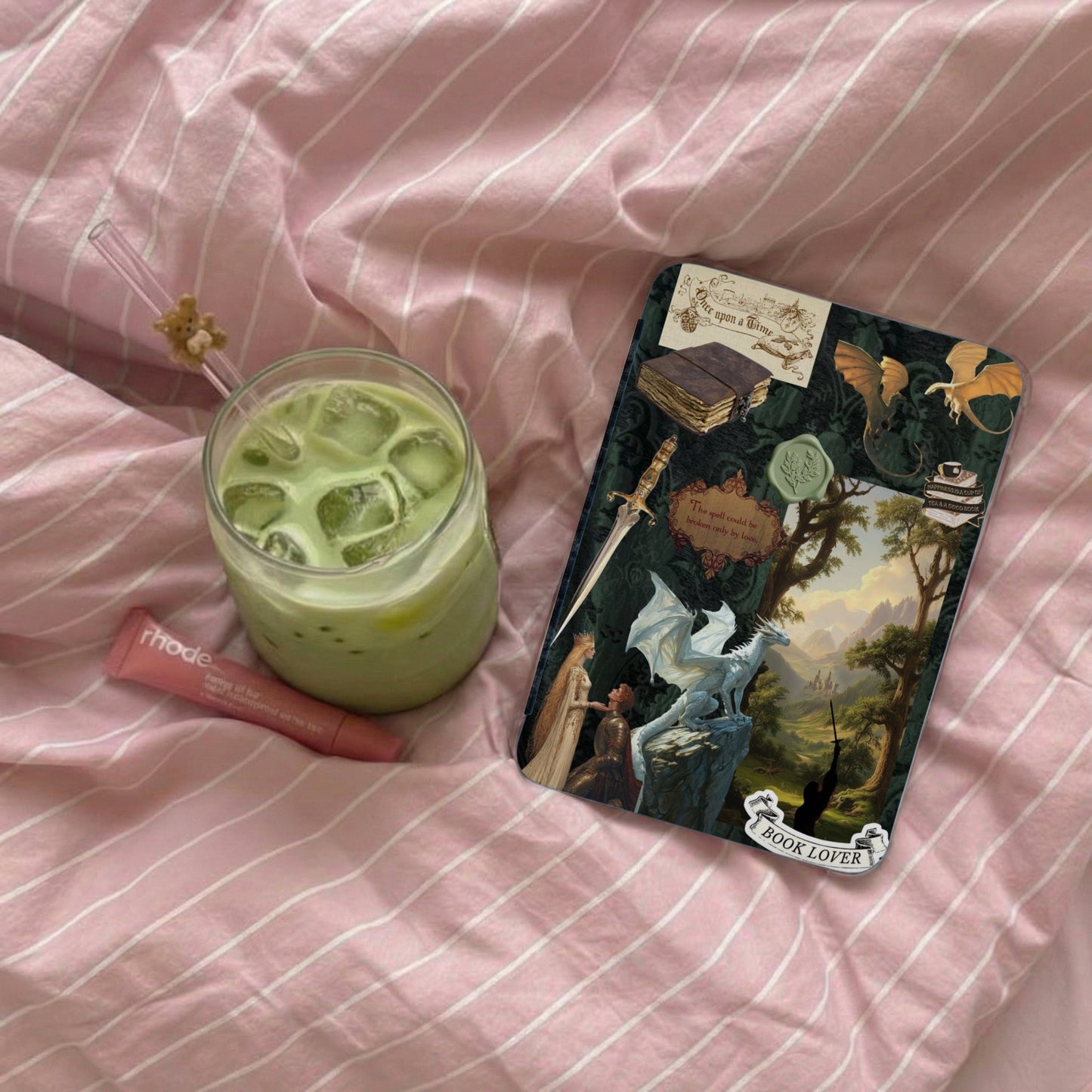 A matcha latte, lip balm, and fantasy-themed "Book Lover" sticker on pink striped fabric.