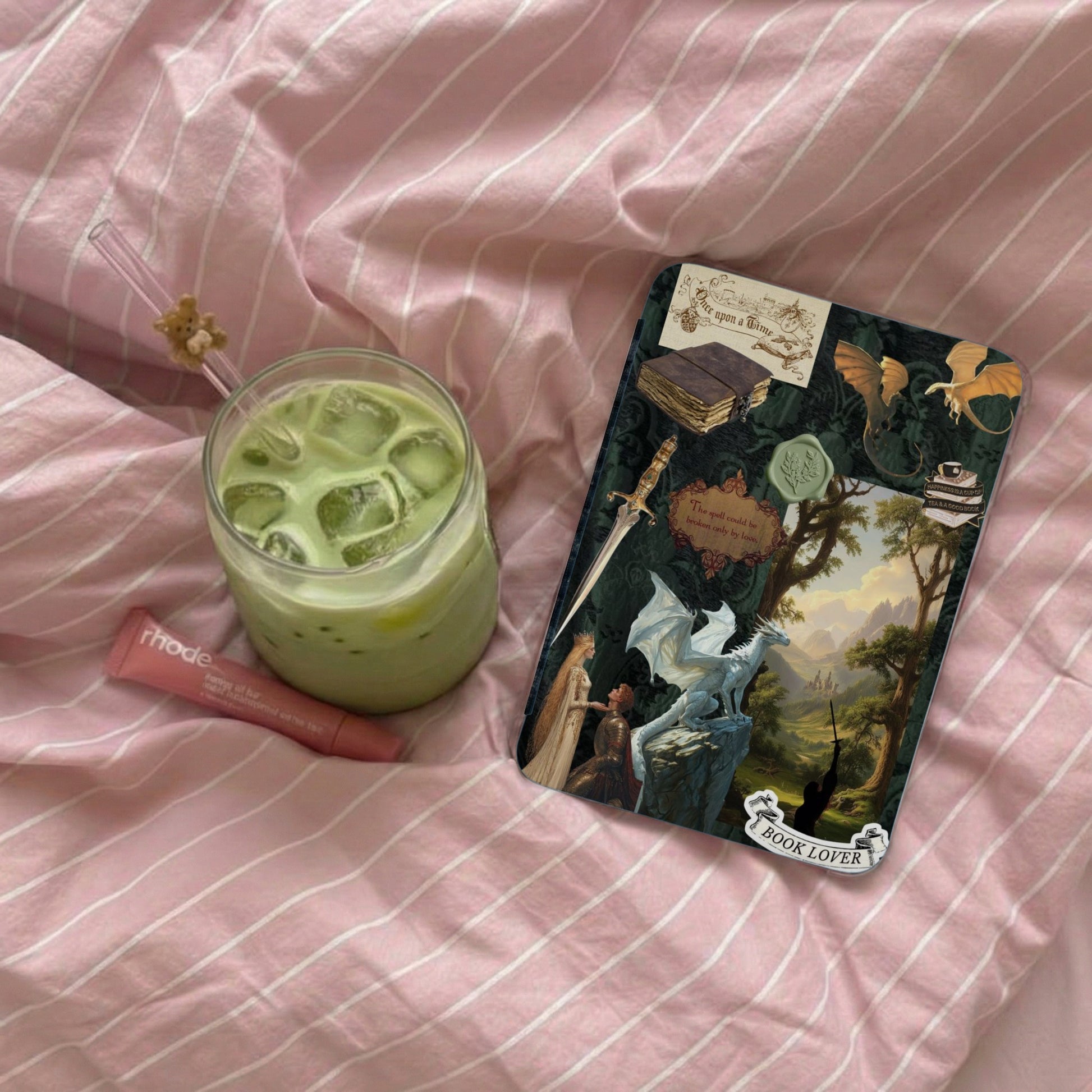A matcha latte, lip balm, and fantasy-themed "Book Lover" sticker on pink striped fabric.