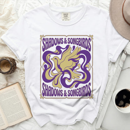 White Comfort Colors t-shirt with purple and gold "Shadows & Songbirds" graphic.