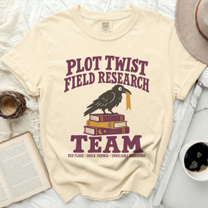 Cream t-shirt with "Plot Twist Field Research Team" text and a crow on books.