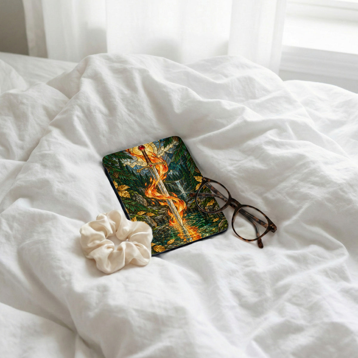 Rectangular case with a sword on fire in a forest scene, next to glasses and scrunchie.