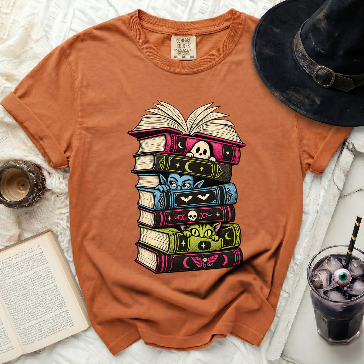 Orange t-shirt with stacked Halloween-themed books featuring a ghost, vampire, cat, and moth.