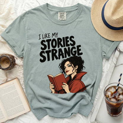 Light blue t-shirt with "I Like My Stories Strange" and a woman reading
