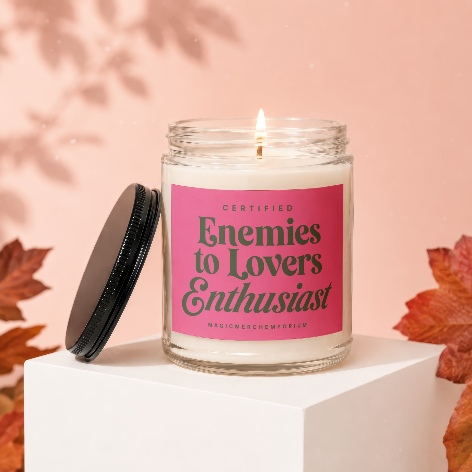A lit candle with a pink label saying "Certified Enemies to Lovers Enthusiast".