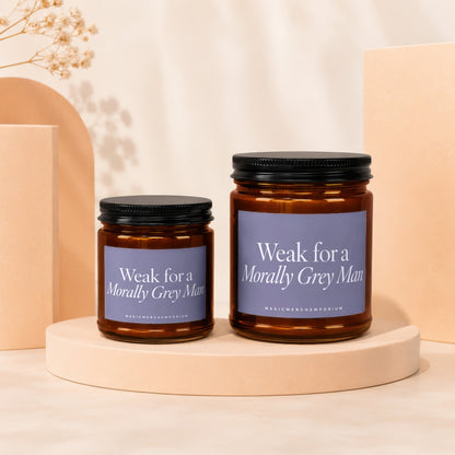 Two amber glass candles with black lids and purple labels reading "Weak for a Morally Grey Man".