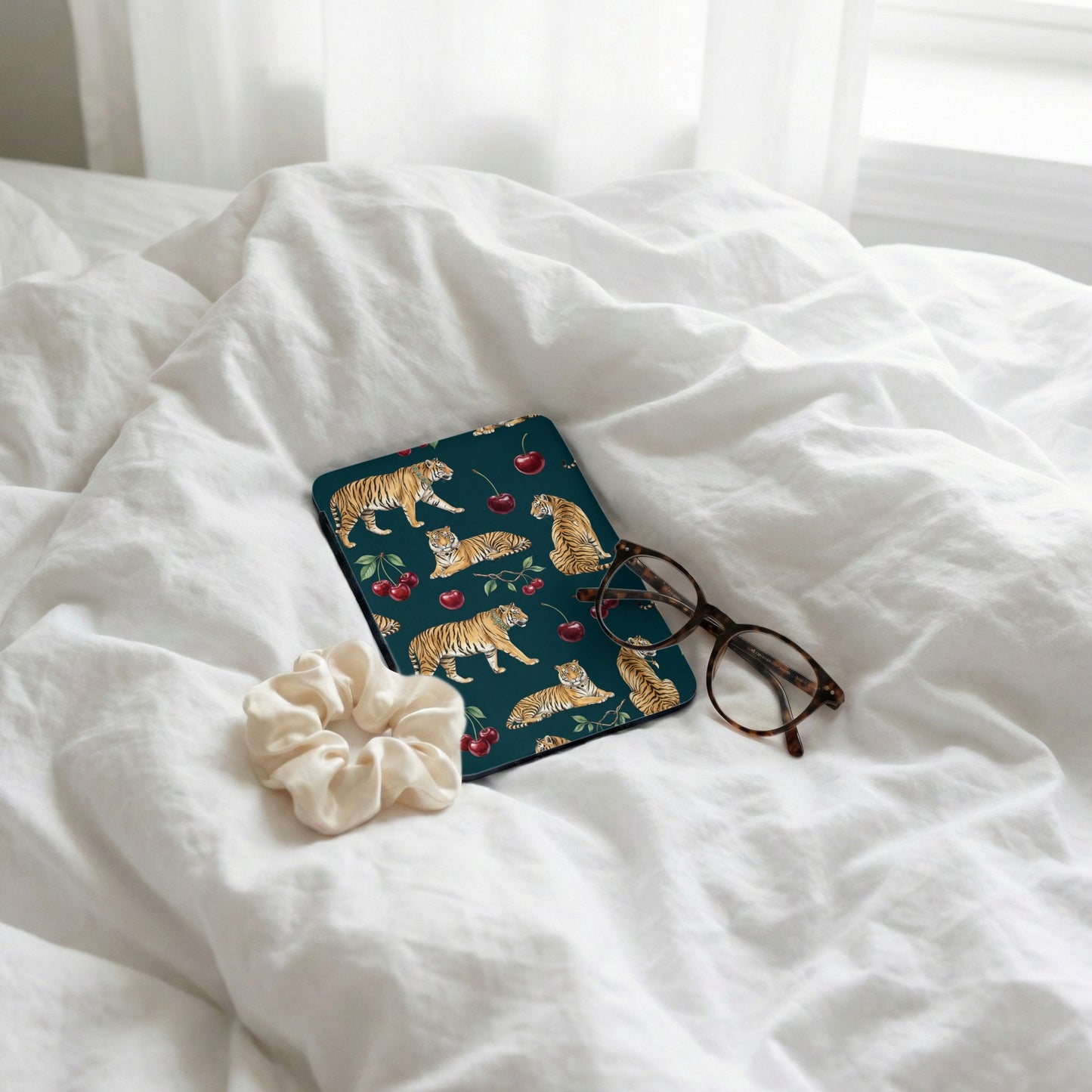Dark teal case with tigers and cherries, scrunchie, and glasses on white sheets.