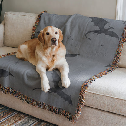 A golden retriever dog is sitting on a gray blanket with a dragon design, which is placed on a beige couch.