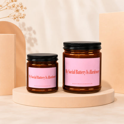 Two amber glass jars with black lids and pink labels reading "My Social Battery Is Hardcover."