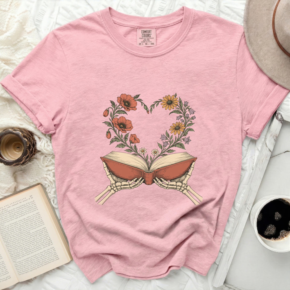 Pink t-shirt with skeleton hands holding an open book with flowers forming a heart.