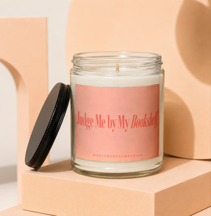 Glass candle with peach label reading "Judge Me by My Bookshelf."