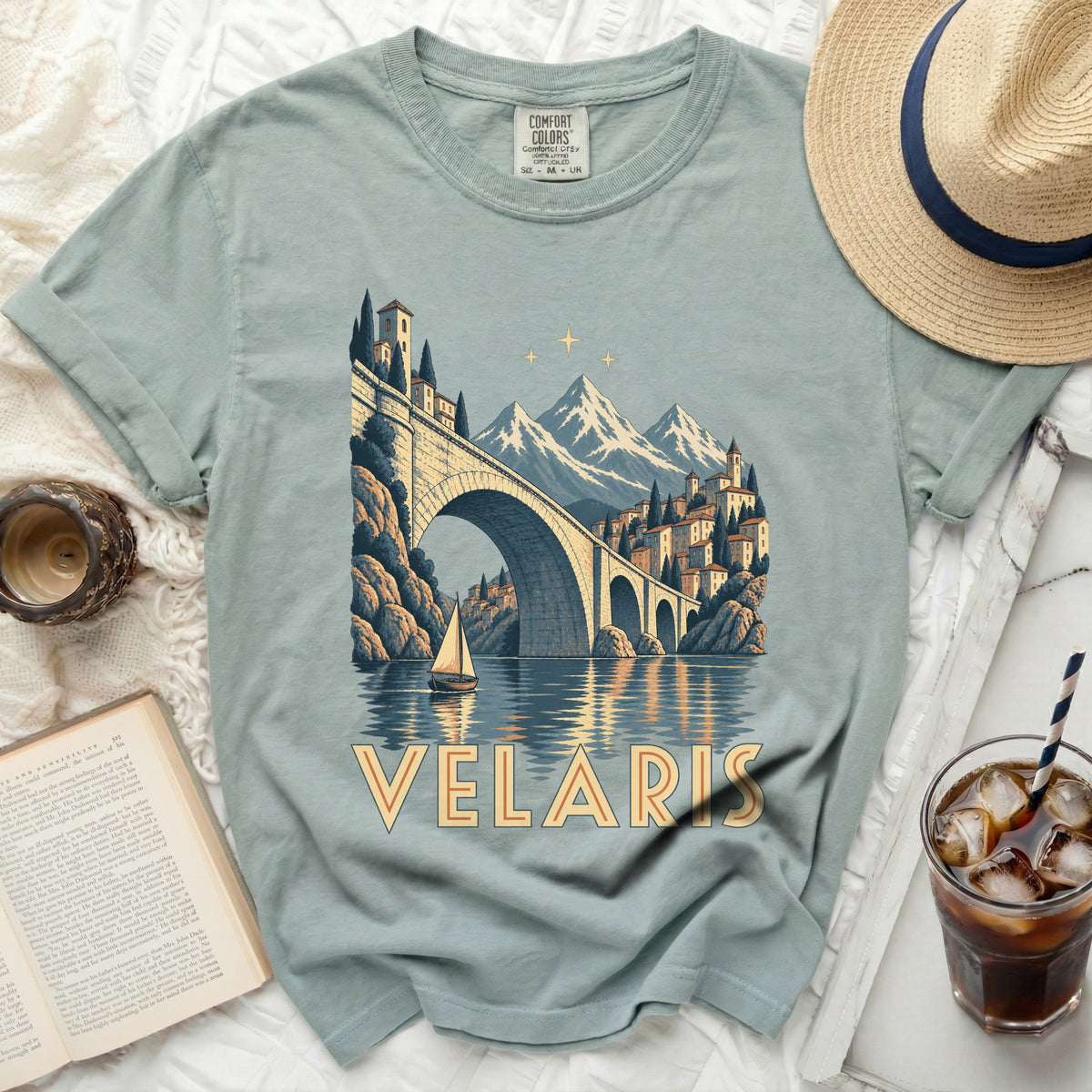 T-shirt with a scenic print of a bridge, buildings, mountains, and a sailboat, and the text "VELARIS".
