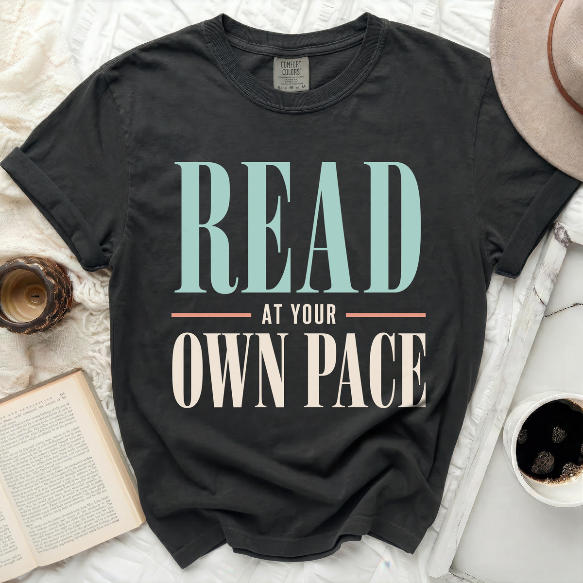 Black Comfort Colors t-shirt with "READ AT YOUR OWN PACE" graphic.