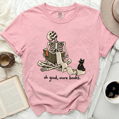 Pink t-shirt with skeleton reading a long scroll and a black cat saying "oh good, more books."