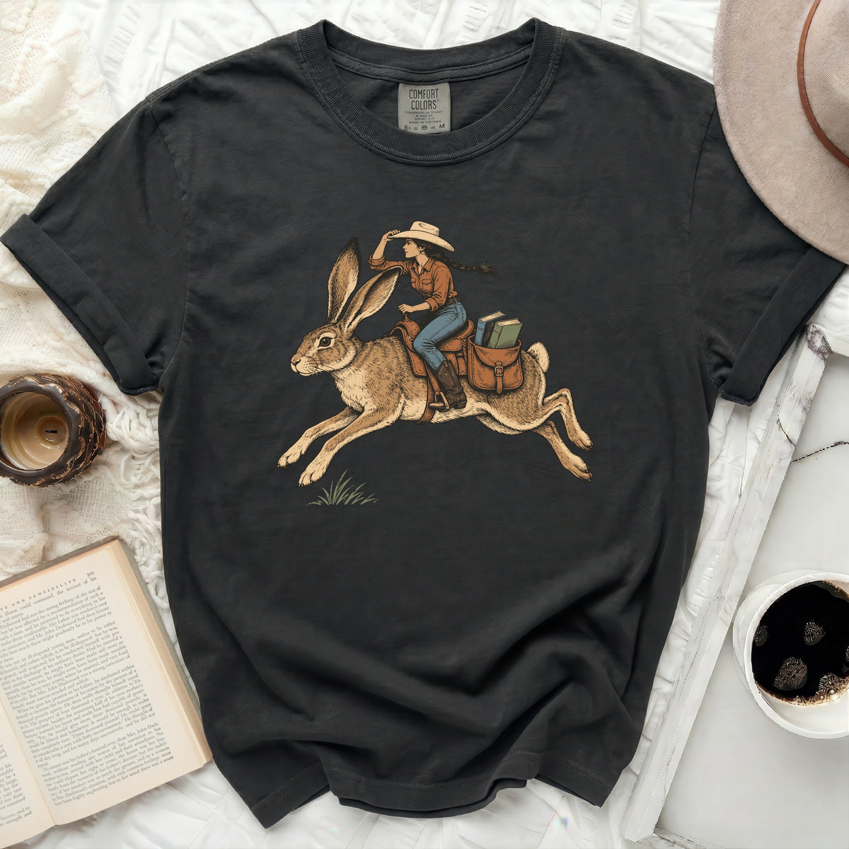 T-shirt with graphic of woman in cowboy hat riding a rabbit with books.