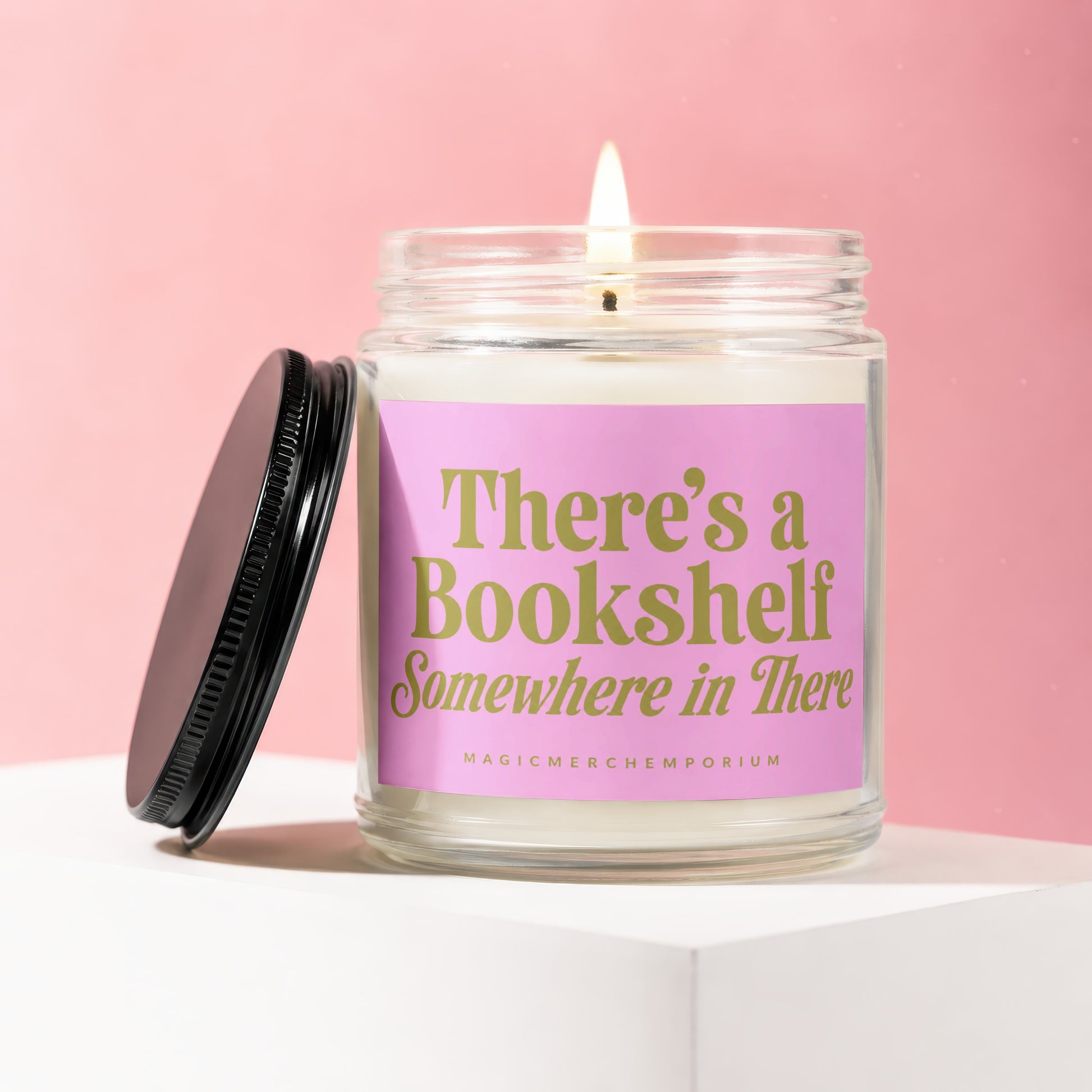 Glass jar candle with pink label reading "There's a Bookshelf Somewhere in There".