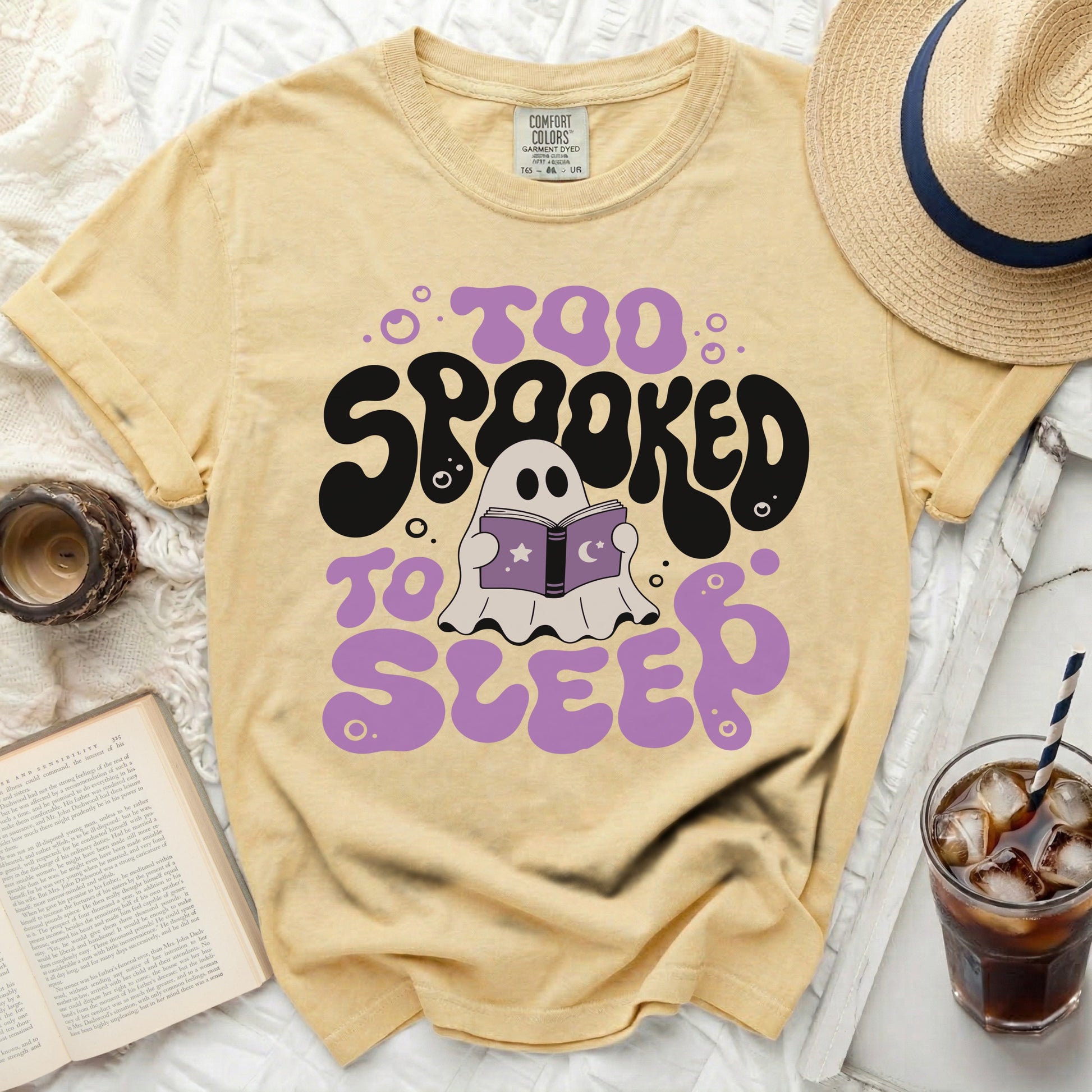 Light yellow t-shirt with "Too Spooked to Sleep" text and a ghost reading a book.
