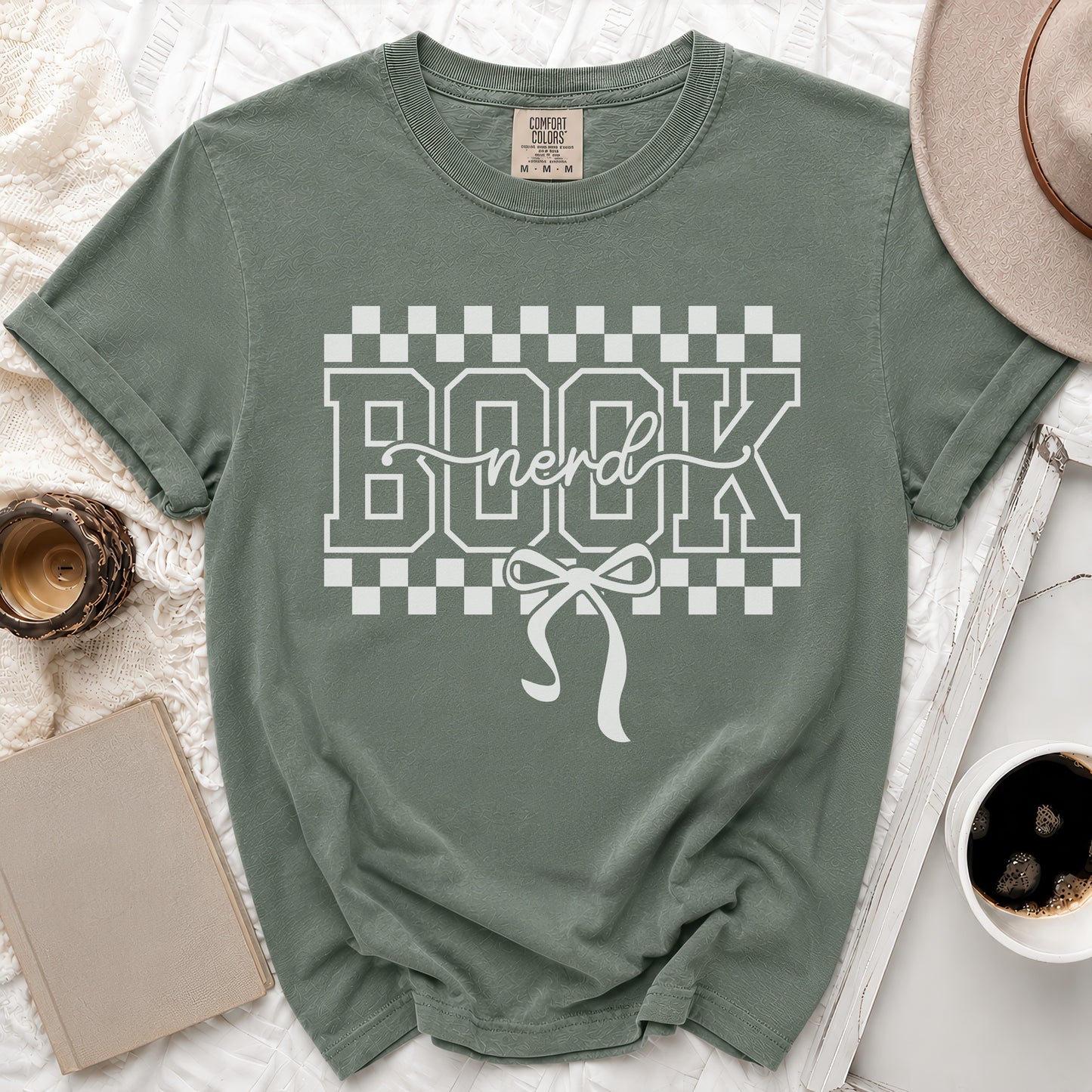 Green t-shirt with white "Book nerd" text and bow graphic on checkered background.
