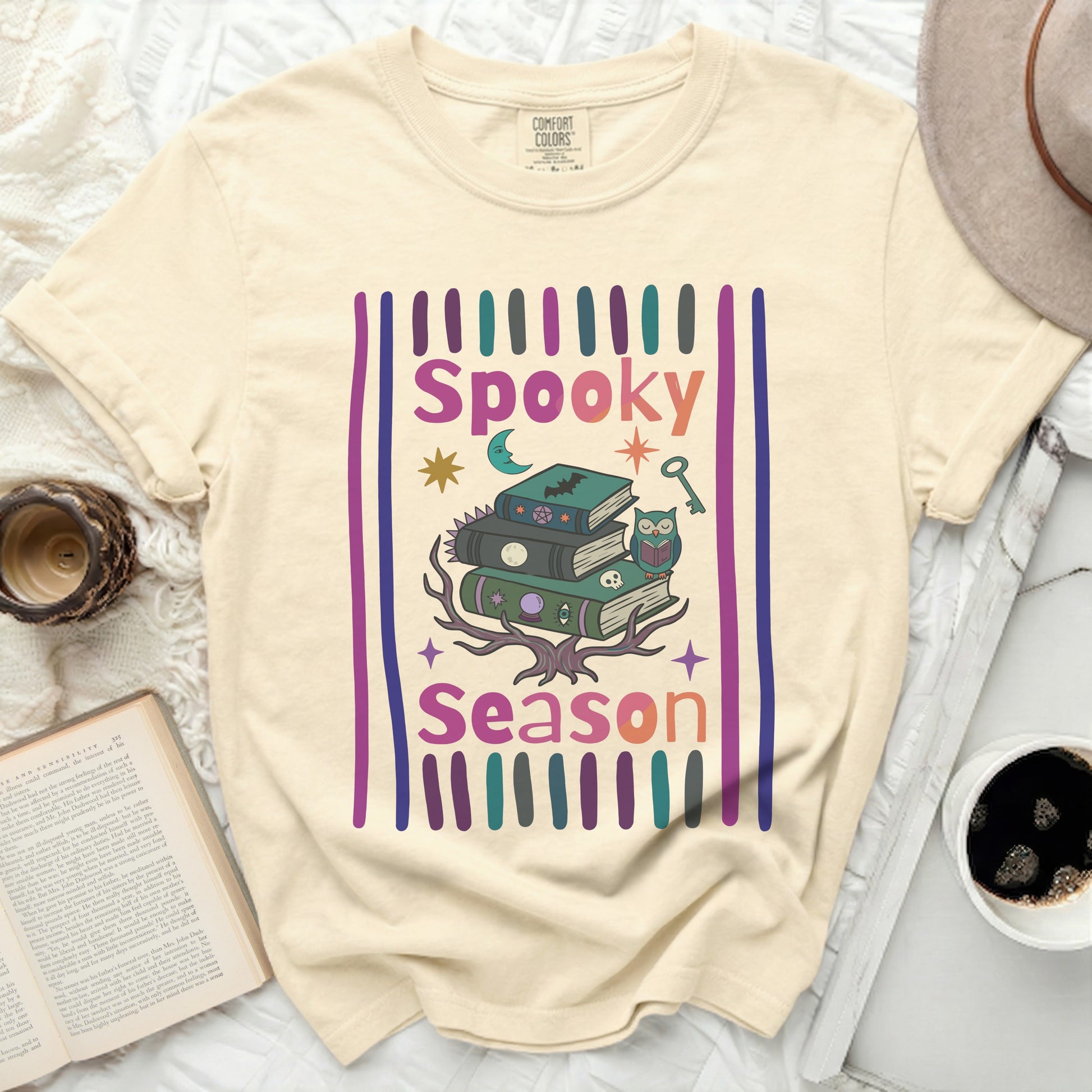 Cream t-shirt with a graphic of stacked books, owl, moon, and text "Spooky Season."