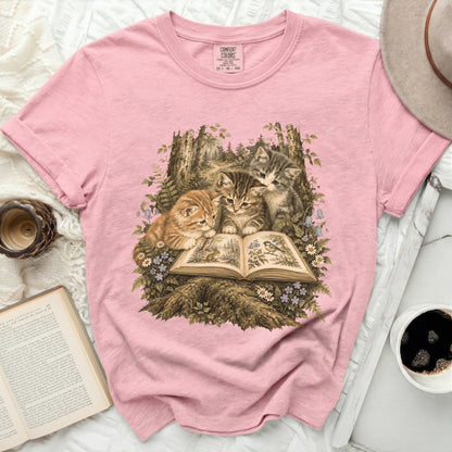 Pink t-shirt with kittens reading a forest scene on an open book.