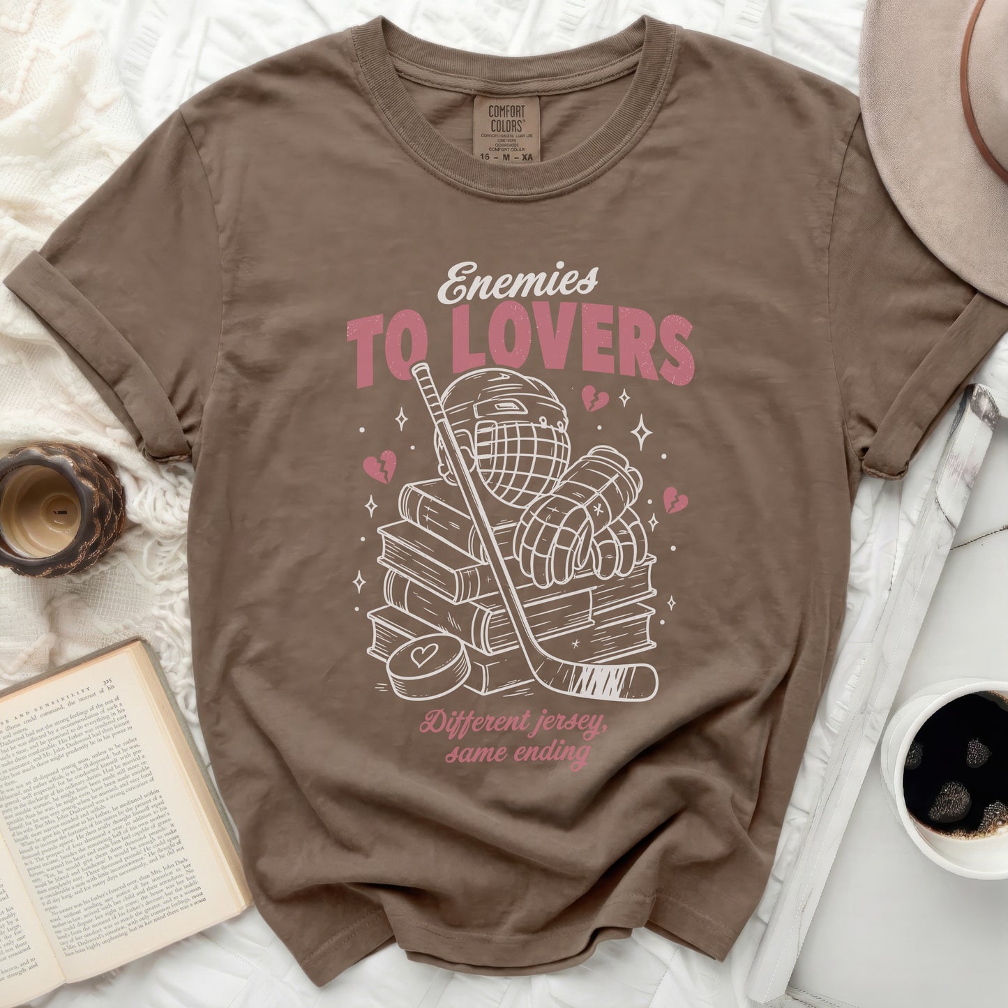 T-shirt with "Enemies To Lovers" text, hockey gear, and books.