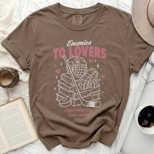 T-shirt with "Enemies To Lovers" text, hockey gear, and books.