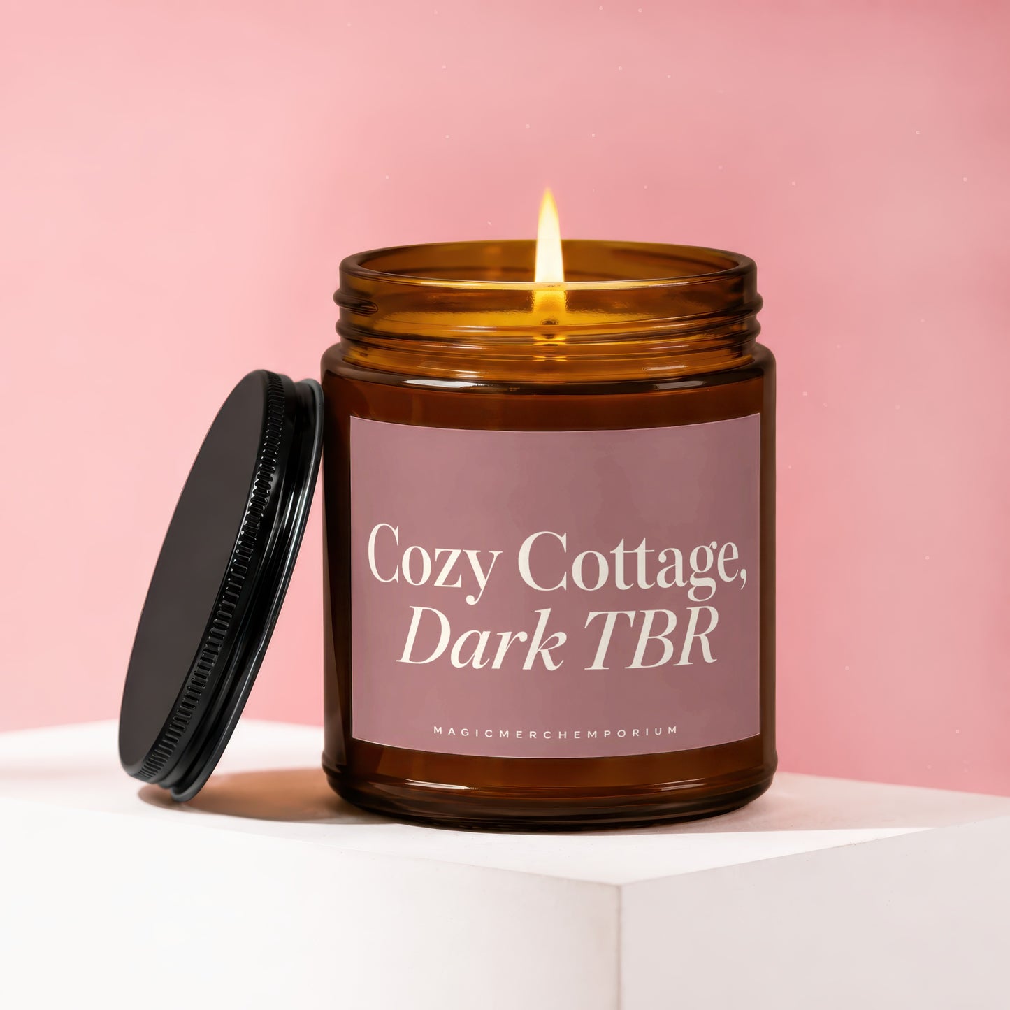 Amber jar candle with lit flame, labeled "Cozy Cottage, Dark TBR," lid off.