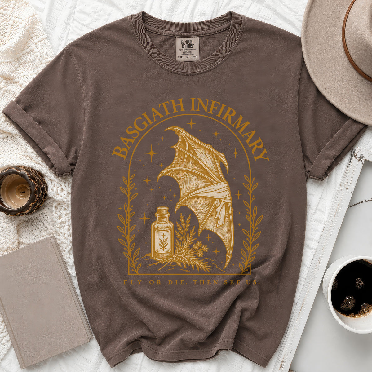 Brown t-shirt featuring a gold graphic of a dragon wing, a potion bottle, and the text Basgiath Infirmary.