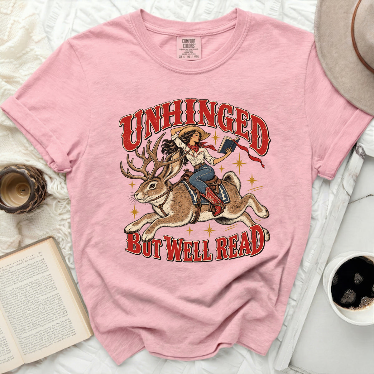 Pink t-shirt with "Unhinged But Well Read" graphic of woman on rabbit.