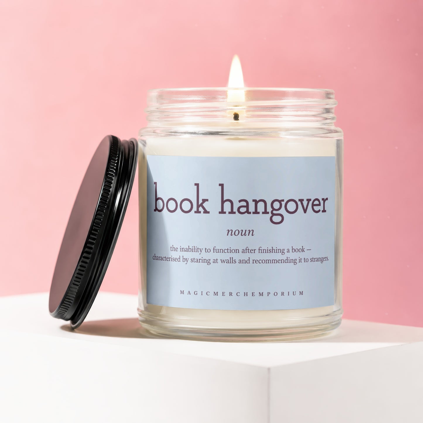 Glass candle with lit wick, labeled "book hangover noun" with definition and brand name.