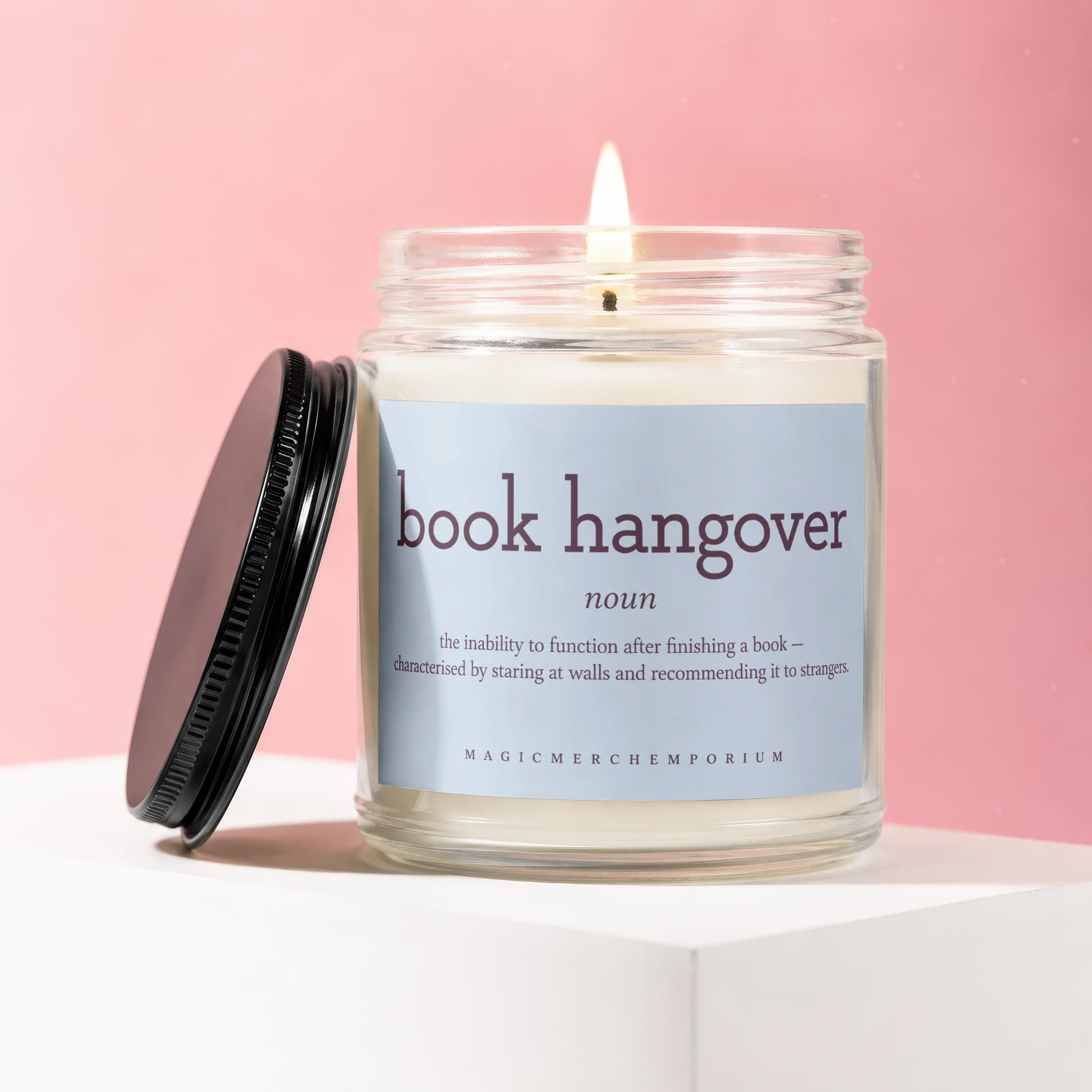Glass candle with lit wick, labeled "book hangover noun" with definition and brand name.