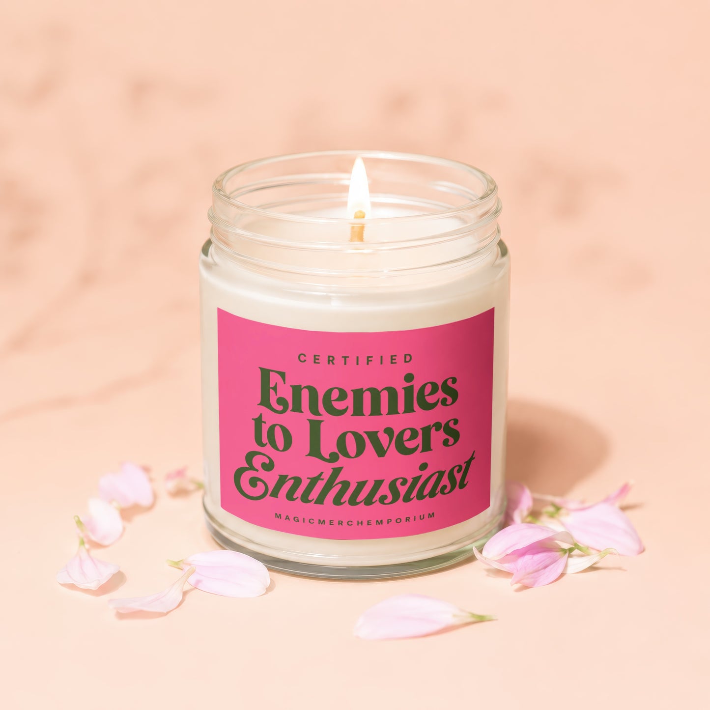 Candle with pink label reading "Certified Enemies to Lovers Enthusiast" surrounded by petals.
