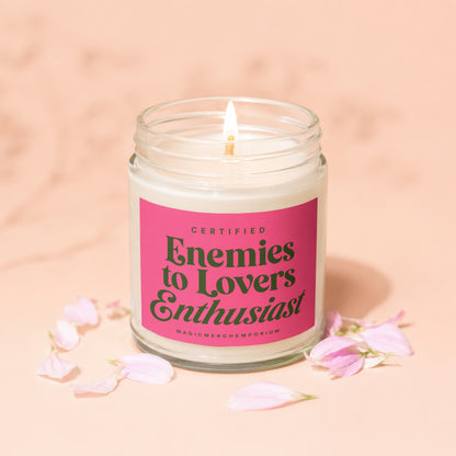 Candle with pink label reading "Certified Enemies to Lovers Enthusiast" surrounded by petals.