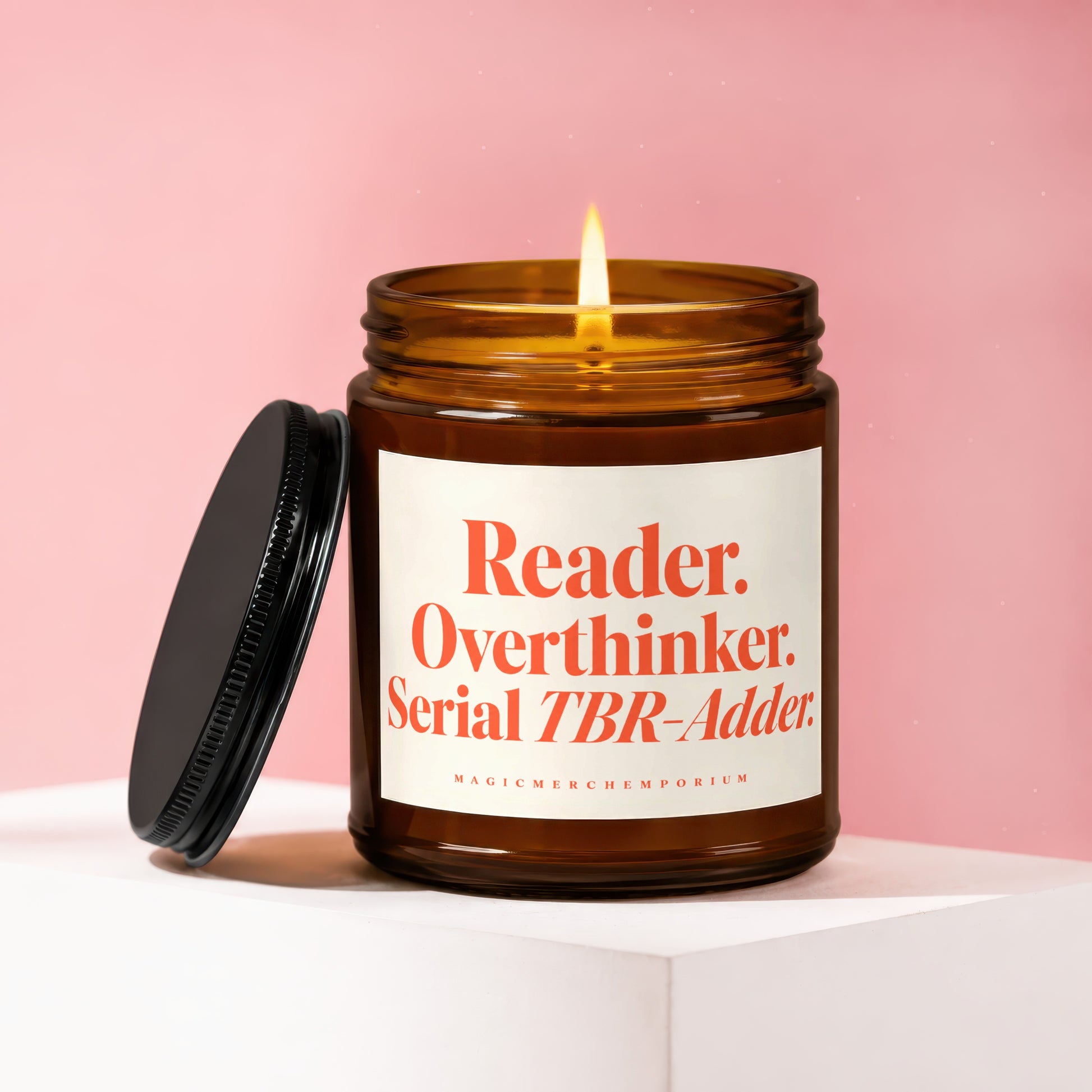 Amber jar candle with lit wick and black lid, reading "Reader. Overthinker. Serial TBR-Adder."