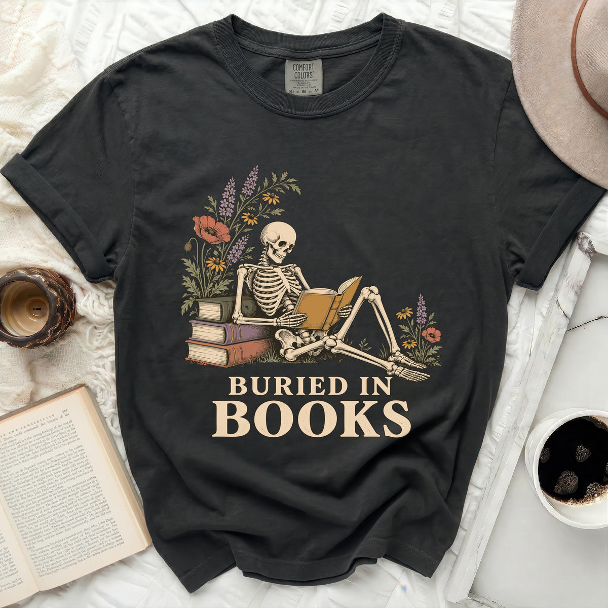 Skeleton sitting and reading a book with text "BURIED IN BOOKS".