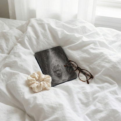 Book with leopard design, glasses, and scrunchie on white crinkled sheets.