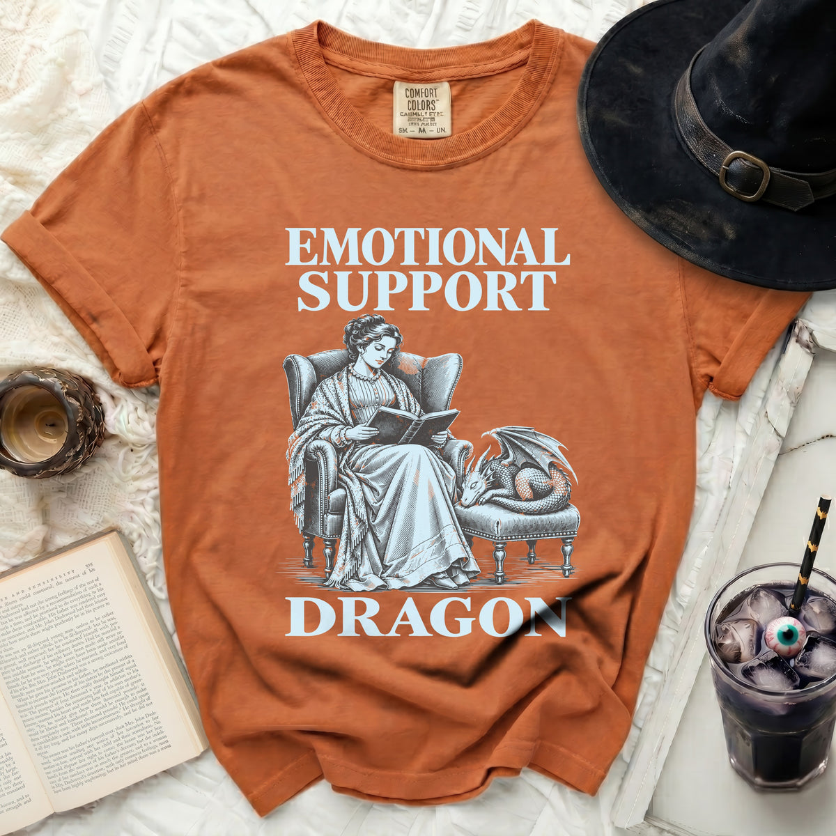 Orange t-shirt with text "Emotional Support Dragon" and an illustration of a woman reading to a dragon.