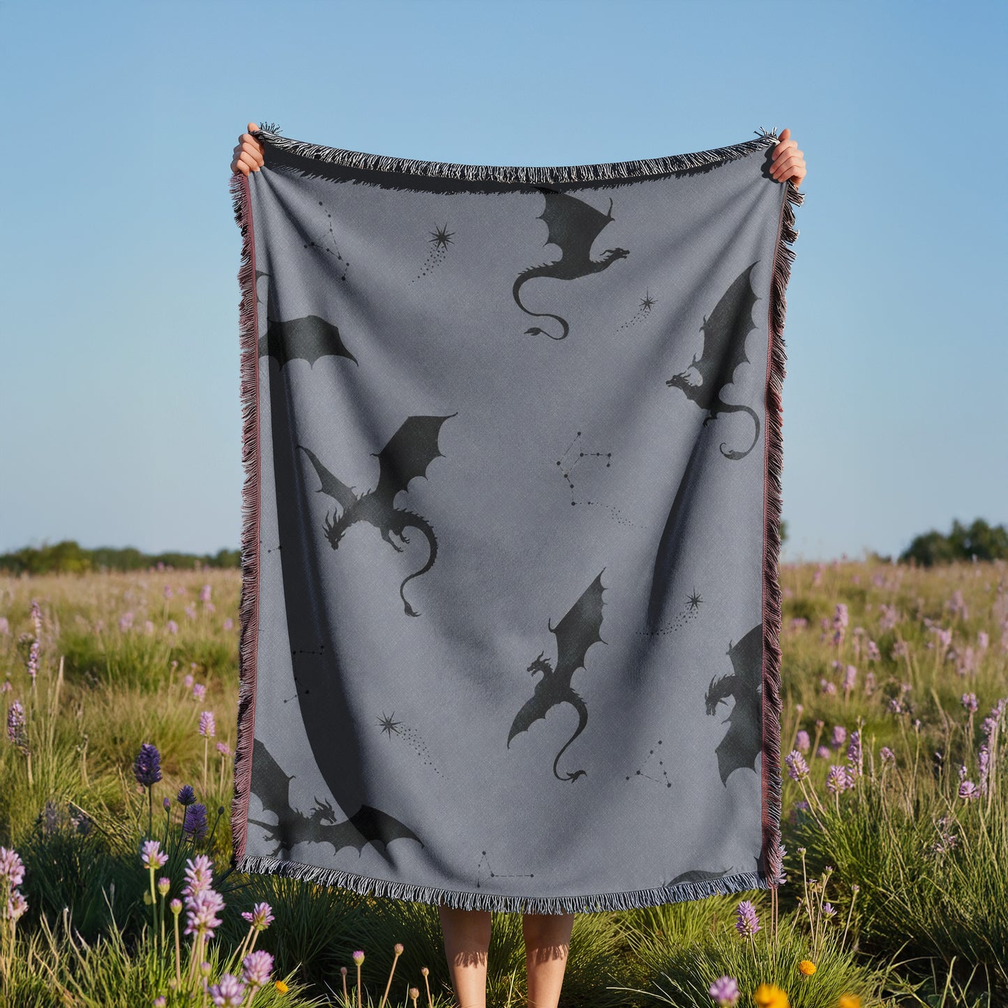 A person is holding up a gray blanket with black dragon silhouettes against a field of purple flowers.