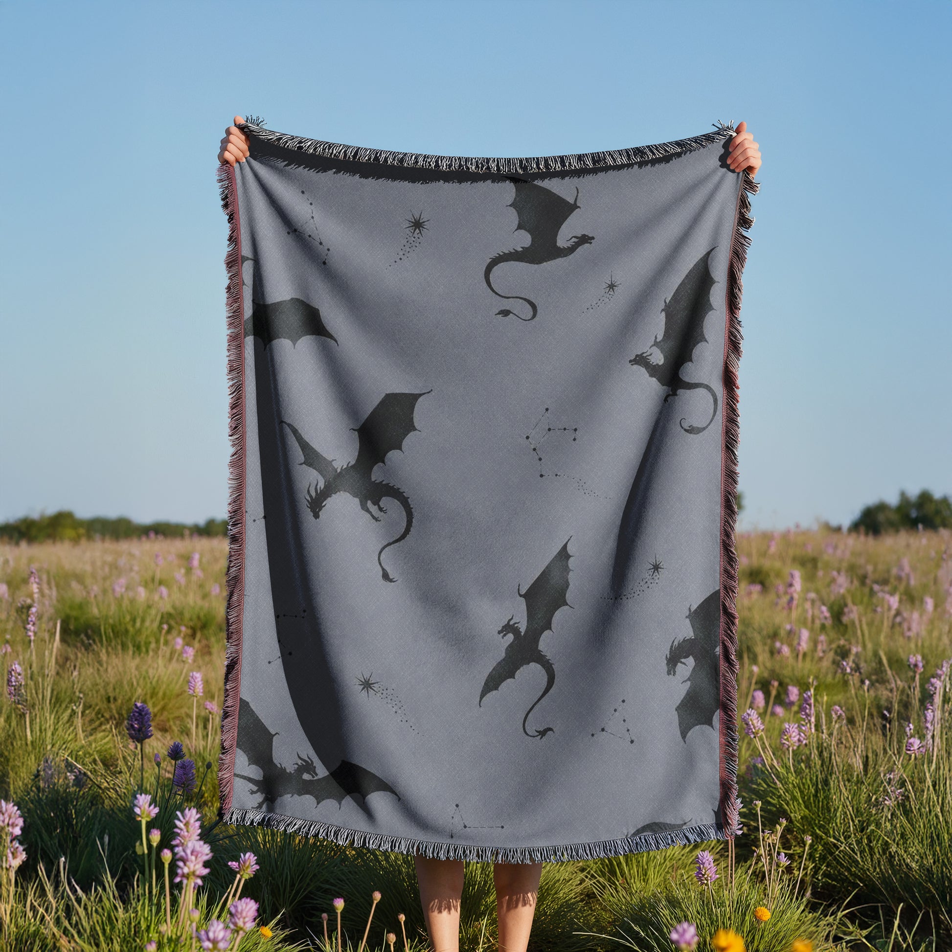 A person is holding up a gray blanket with black dragon silhouettes against a field of purple flowers.