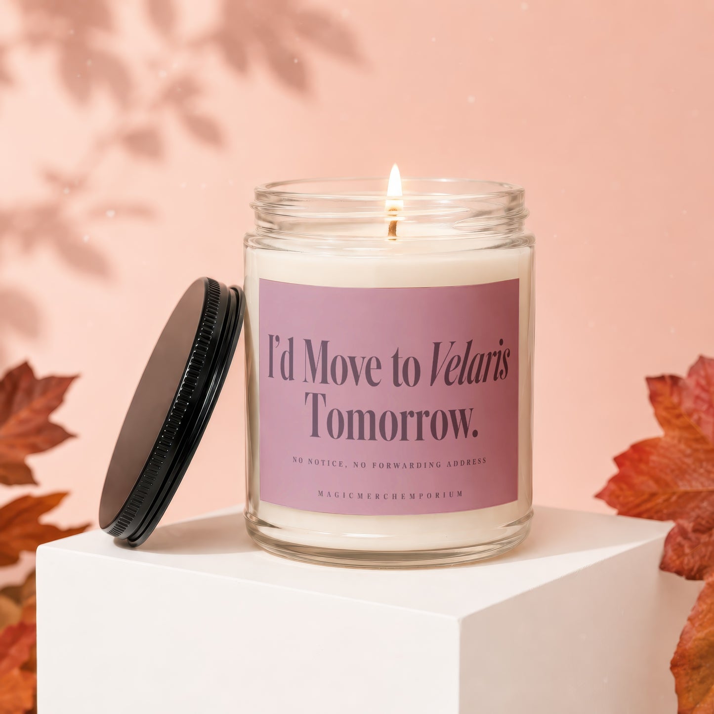 A lit candle in a glass jar with a pink label reads I'd Move to Velaris Tomorrow.