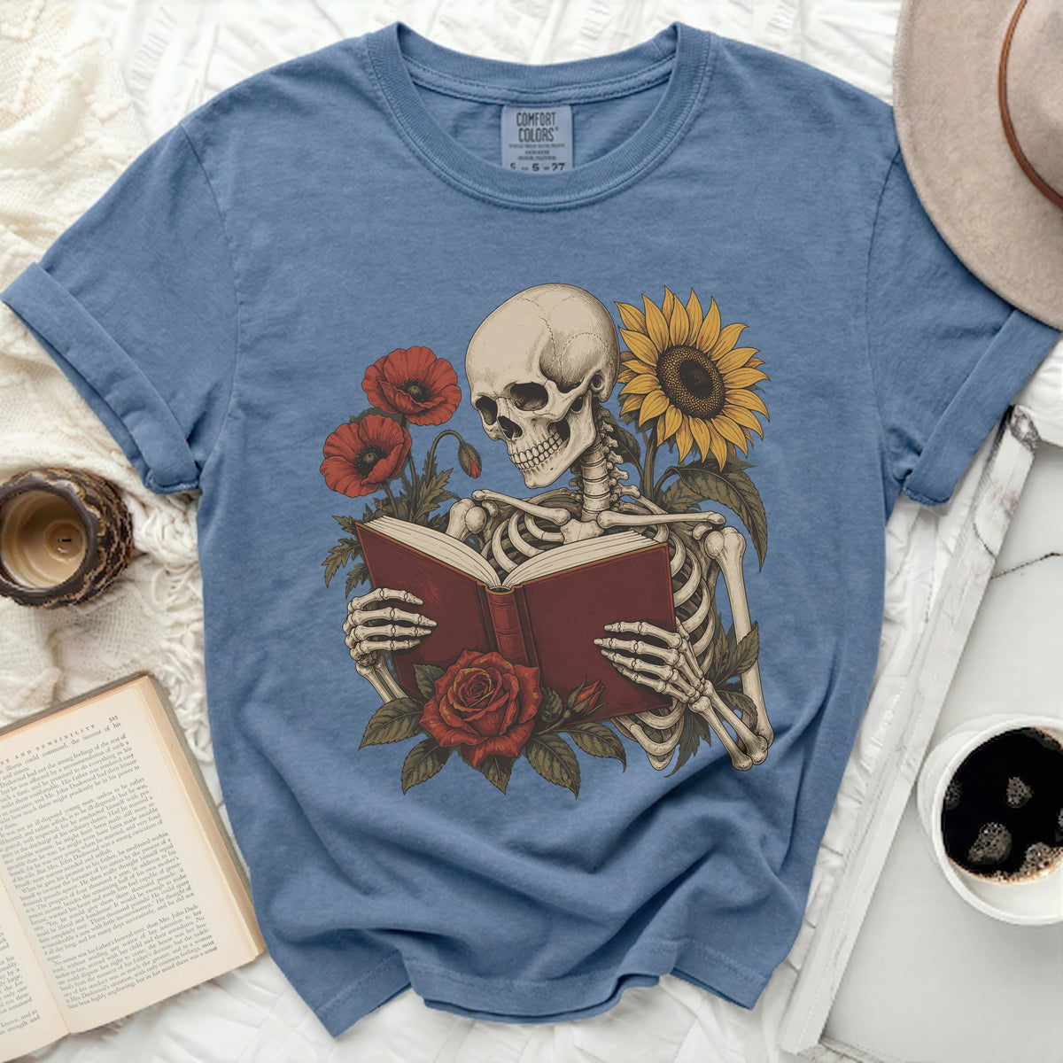 Skeleton reading a book surrounded by poppies, a rose, and a sunflower.