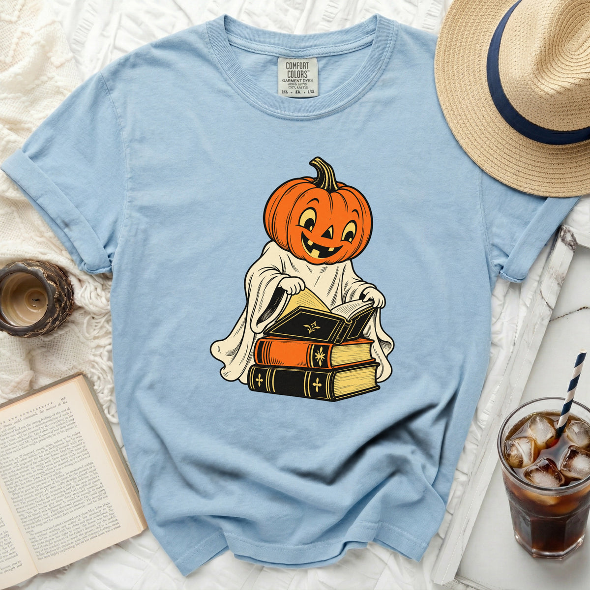 Light blue t-shirt with a graphic of a pumpkin ghost reading books.