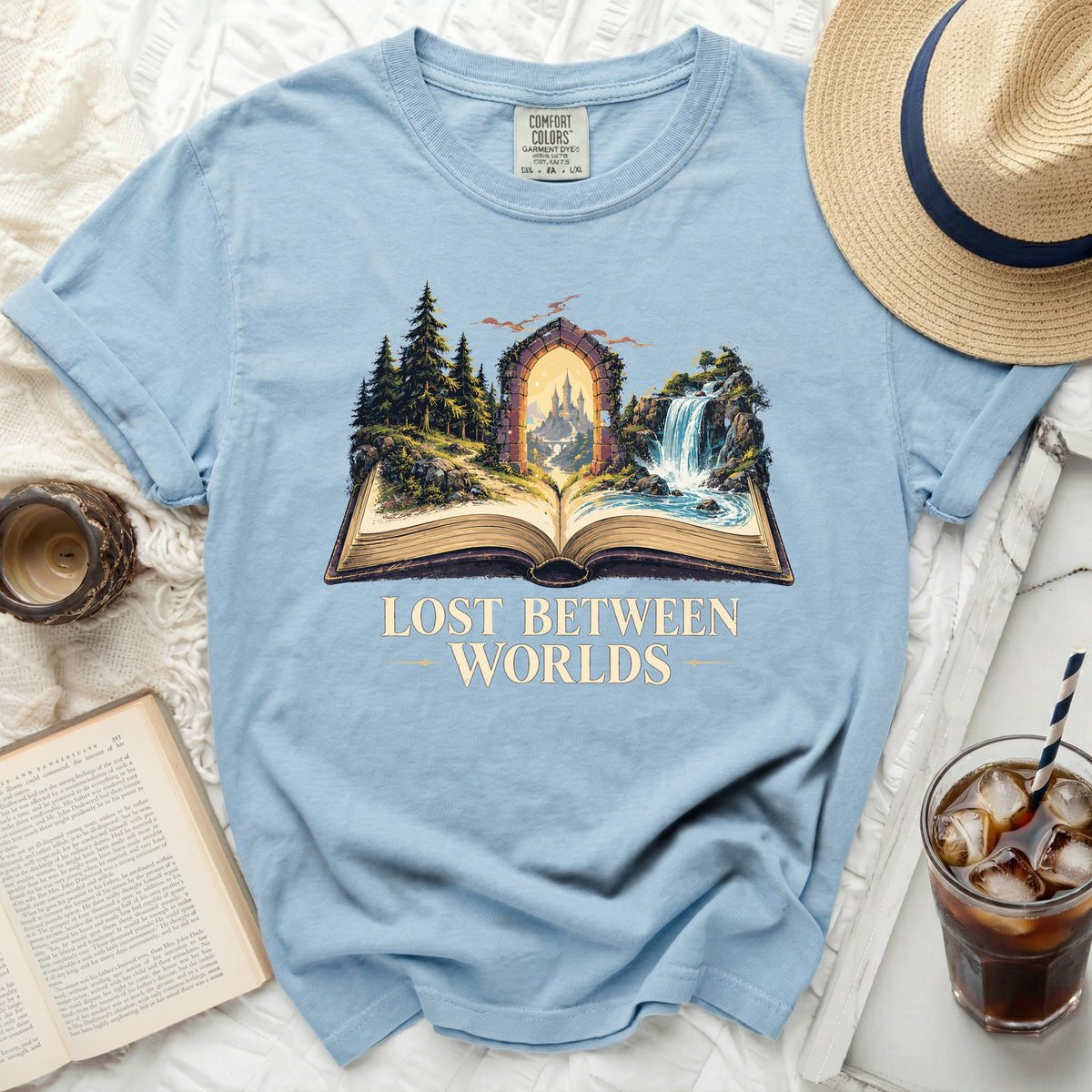 Light blue t-shirt with "Lost Between Worlds" graphic depicting an open book with fantasy landscape.