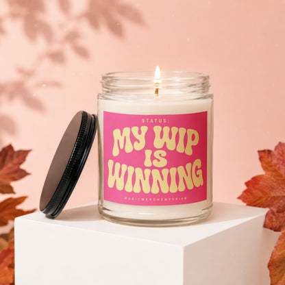 Lit glass candle with hot pink label reading "My WIP is Winning" on a white pedestal.