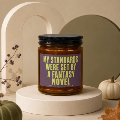 Candle with text "My Standards Were Set By A Fantasy Novel" on purple label.