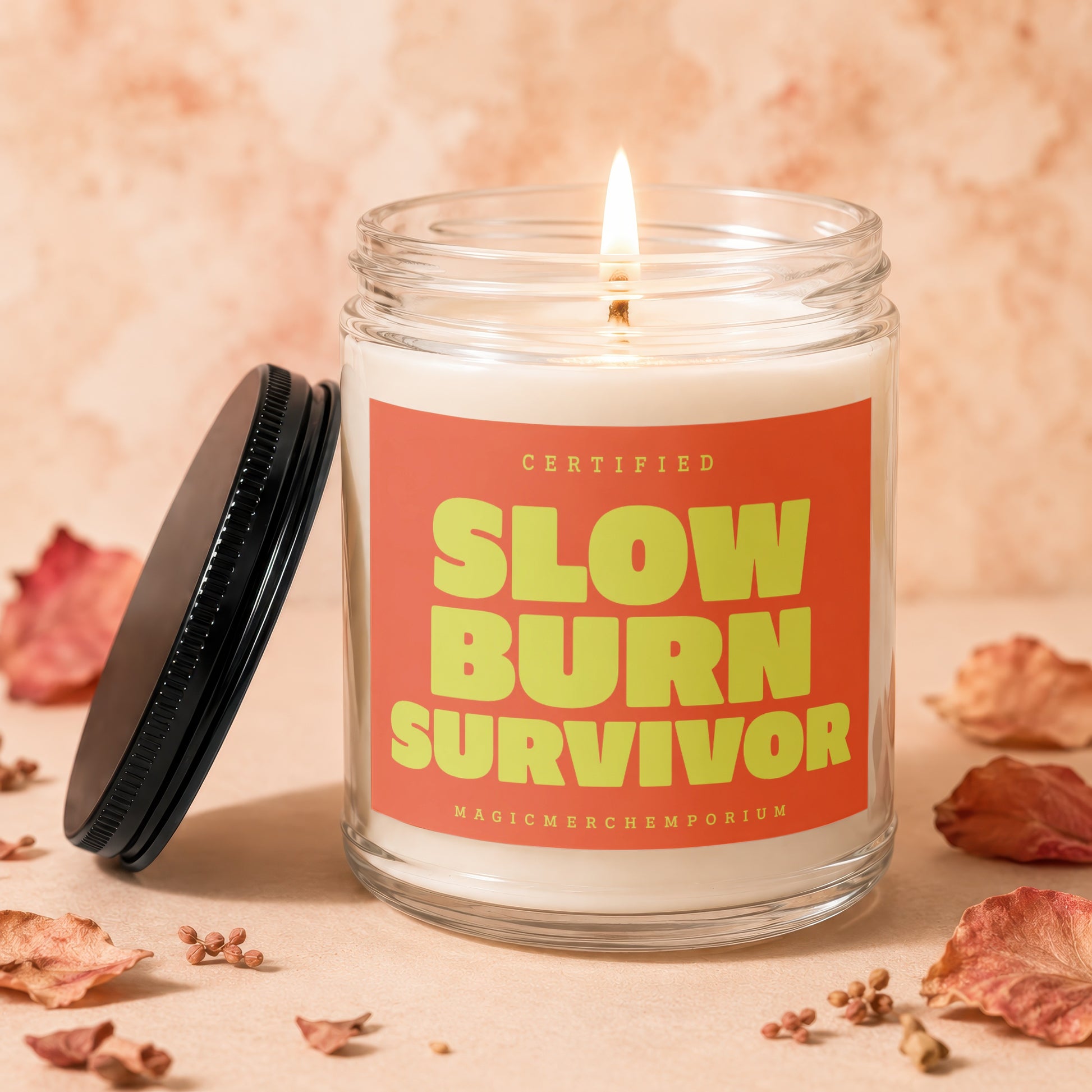 Lit candle in glass jar with orange label reading "Certified Slow Burn Survivor".
