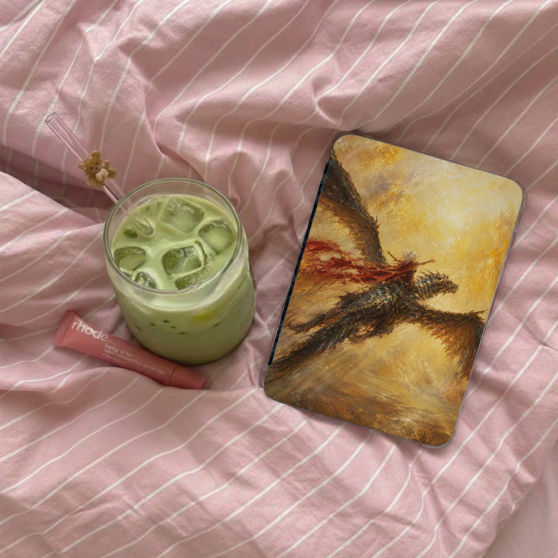 Laptop case with a dragon rider artwork, next to matcha ice drink and lip balm.