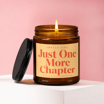 Amber glass candle with lit flame and black lid, text reads "Smells Like Just One More Chapter".