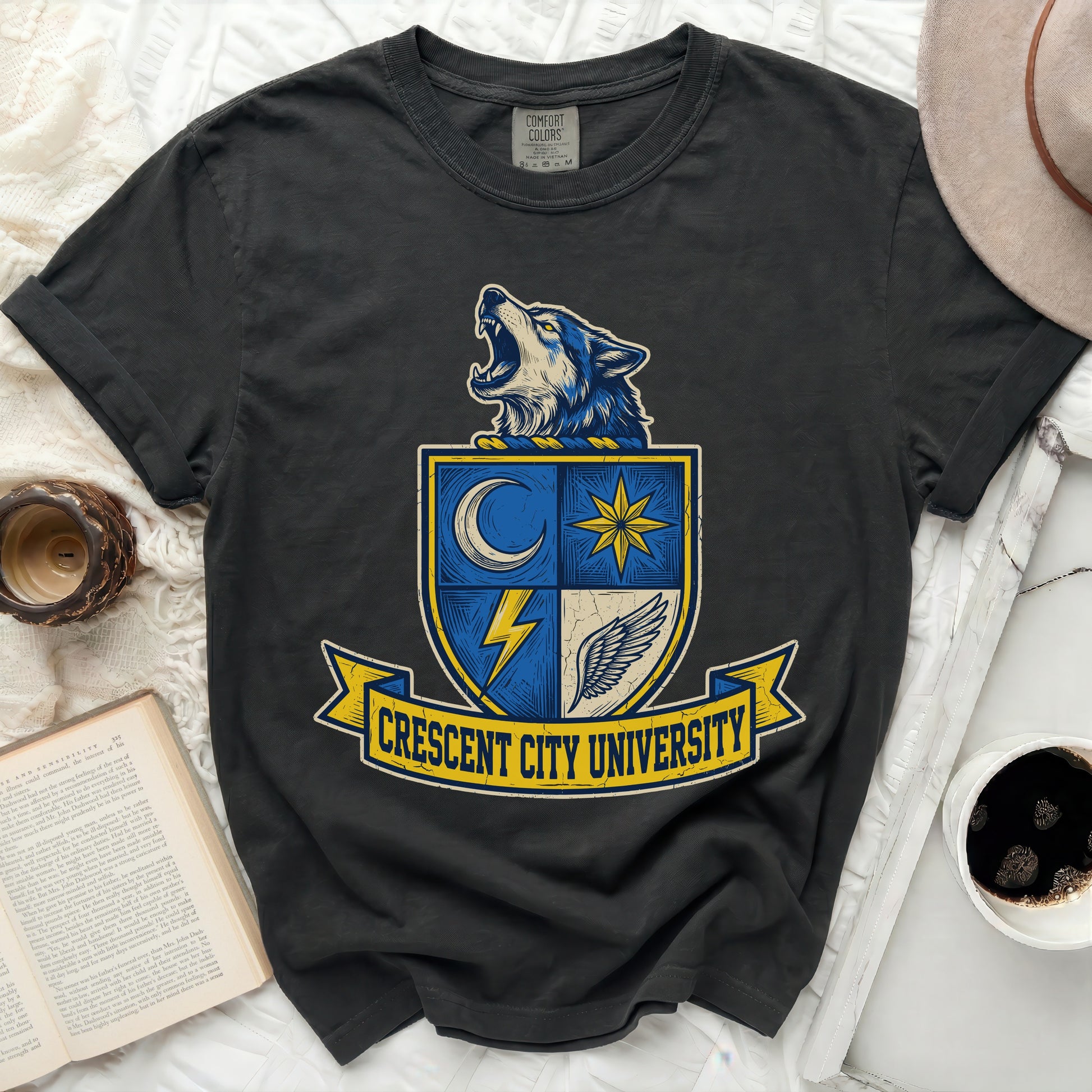 Black t-shirt featuring a shield with a howling wolf, crescent moon, star, and wings. Text reads "CRESCENT CITY UNIVERSITY".